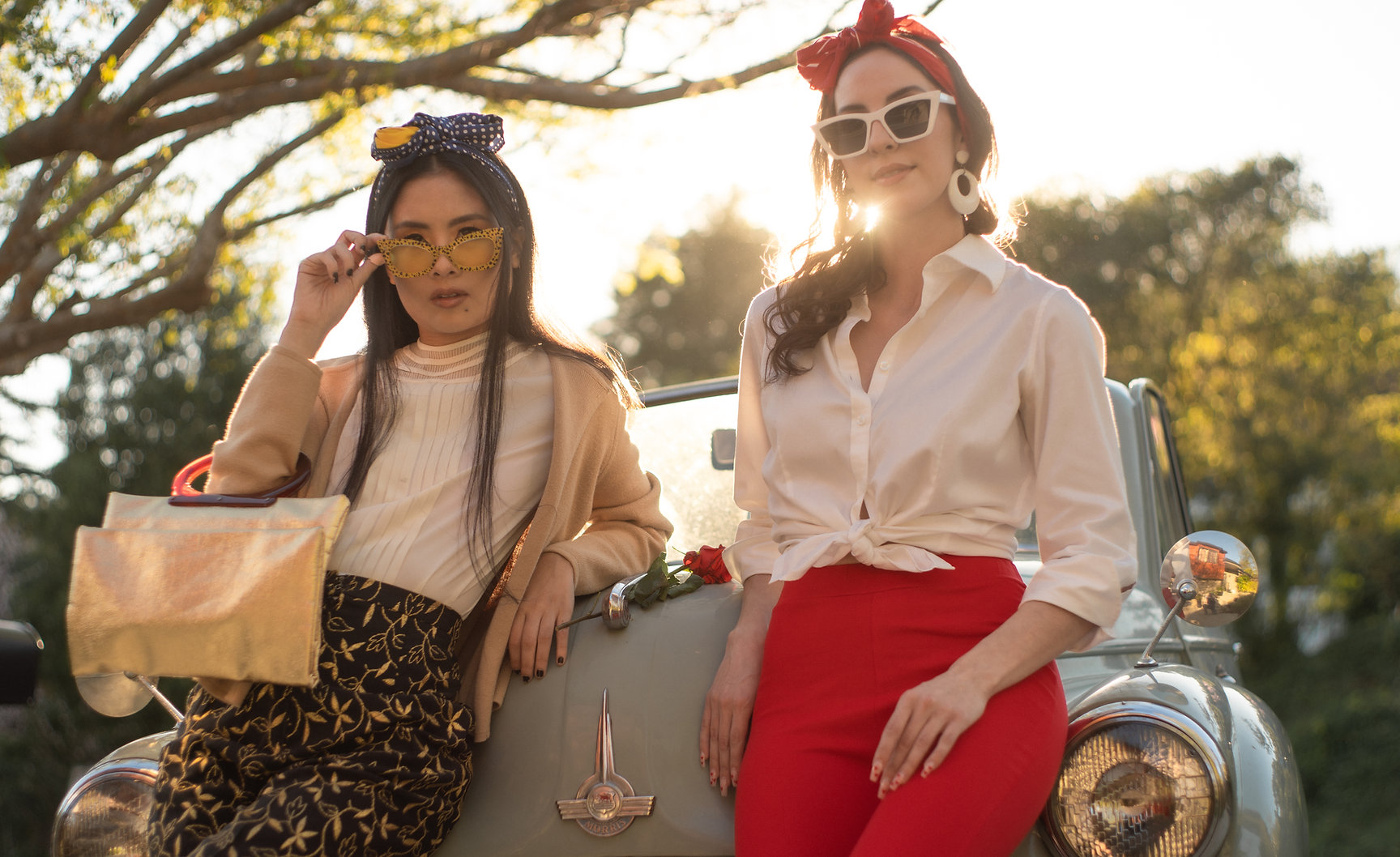 Two women in sunglasses lean on a vintage car
